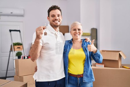 Photo for Hispanic mother and son holding keys of new home smiling happy and positive, thumb up doing excellent and approval sign - Royalty Free Image