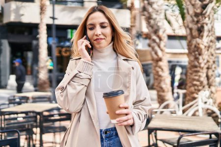 Téléchargez les photos : Jeune femme blonde parlant sur smartphone boire du café à la terrasse du café - en image libre de droit