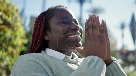 Téléchargez les photos : Femme africaine aux cheveux tressés priant les yeux fermés au parc - en image libre de droit