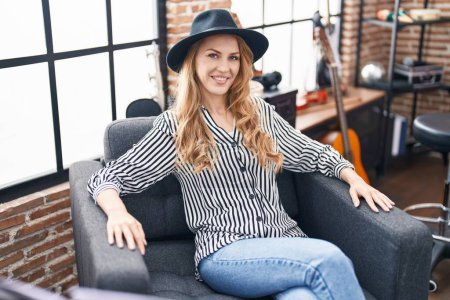 Téléchargez les photos : Jeune femme blonde musicienne souriante confiante assise sur un canapé au studio de musique - en image libre de droit