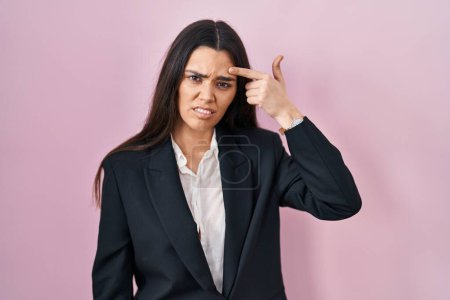 Téléchargez les photos : Jeune femme brune portant un style d'affaires sur fond rose pointant malheureux de boutons sur le front, infection laide de la tête noire. acné et problème de peau - en image libre de droit