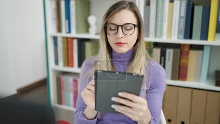 Téléchargez les photos : Young blonde woman student using touchpad studying at library university - en image libre de droit
