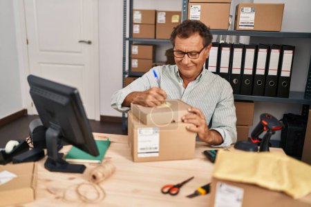 Téléchargez les photos : Middle age man ecommerce business worker writing on package at office - en image libre de droit