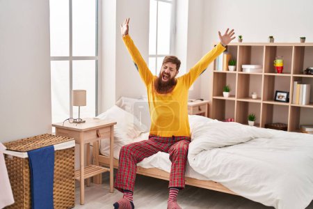 Photo for Young redhead man waking up stretching arms yawning at bedroom - Royalty Free Image