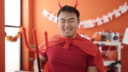 Téléchargez les photos : Young chinese man wearing devil costume holding trident at home - en image libre de droit