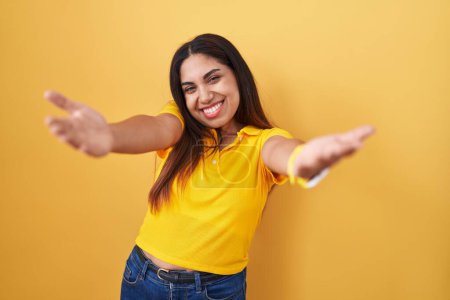 Téléchargez les photos : Jeune femme arabe debout sur fond jaune souriant joyeuse offrant des mains donnant assistance et acceptation. - en image libre de droit