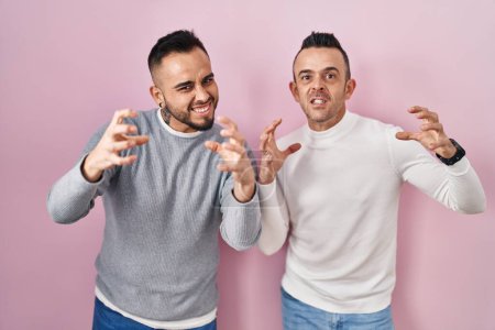 Photo for Homosexual couple standing over pink background shouting frustrated with rage, hands trying to strangle, yelling mad - Royalty Free Image