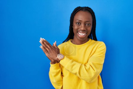 Téléchargez les photos : Belle femme noire debout sur fond bleu applaudissements et applaudissements heureux et joyeux, souriant mains fiers ensemble - en image libre de droit