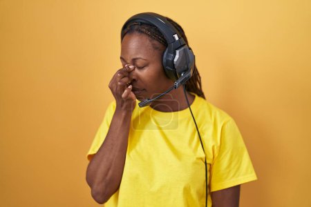 Foto de Mujer afroamericana escuchando música usando auriculares cansados frotando la nariz y los ojos sintiendo fatiga y dolor de cabeza. concepto de estrés y frustración. - Imagen libre de derechos