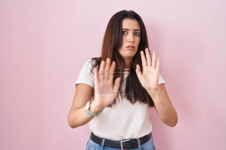 Photo for Young brunette woman standing over pink background moving away hands palms showing refusal and denial with afraid and disgusting expression. stop and forbidden. - Royalty Free Image