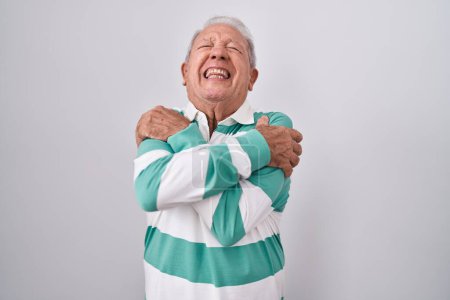 Téléchargez les photos : Homme âgé avec les cheveux gris debout sur fond blanc s'étreignant heureux et positif, souriant confiant. amour de soi et soins de soi - en image libre de droit