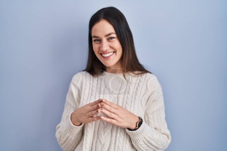 Téléchargez les photos : Young brunette woman standing over blue background hands together and fingers crossed smiling relaxed and cheerful. success and optimistic - en image libre de droit