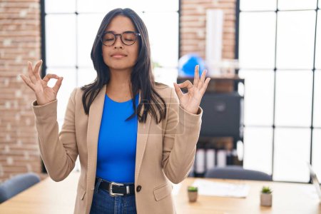 Téléchargez les photos : Femme brune travaillant au bureau portant des lunettes se détendre et sourire les yeux fermés en faisant un geste de méditation avec les doigts. concept de yoga. - en image libre de droit