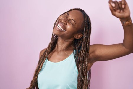 Téléchargez les photos : Femme afro-américaine debout sur fond rose dansant heureux et joyeux, souriant décontracté et confiant écoutant de la musique - en image libre de droit