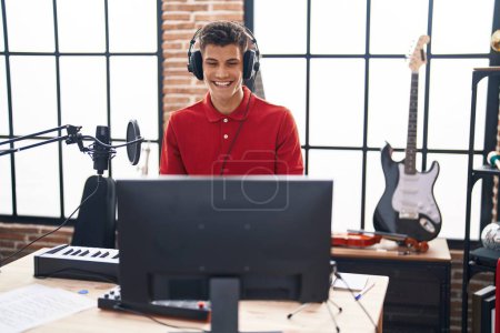 Téléchargez les photos : Jeune homme hispanique jouant du clavier de piano au studio de musique regardant positif et heureux debout et souriant avec un sourire confiant montrant les dents - en image libre de droit