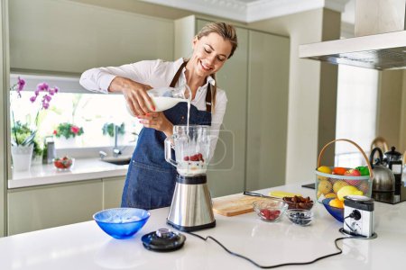 Photo for Young blonde woman smiling confident pouring milk on blender at kitchen - Royalty Free Image