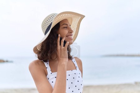 Foto de Young african american woman wearing summer hat talking on smartphone at seaside - Imagen libre de derechos