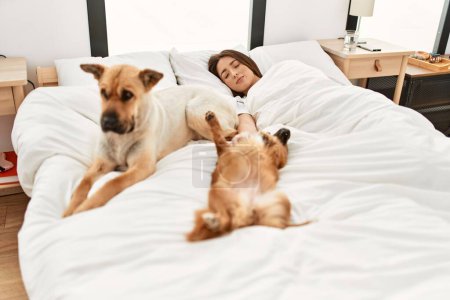 Téléchargez les photos : Jeune femme hispanique dormant couchée sur le lit avec des chiens dans la chambre - en image libre de droit