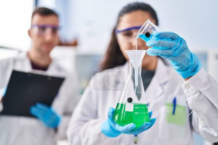 Téléchargez les photos : Man and woman wearing scientist uniform write on document measuring liquid at laboratory - en image libre de droit