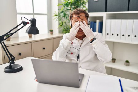 Téléchargez les photos : Médecin-chef travaillant sur rendez-vous en ligne frotter les yeux pour la fatigue et les maux de tête, somnolent et l'expression fatiguée. problème de vision - en image libre de droit