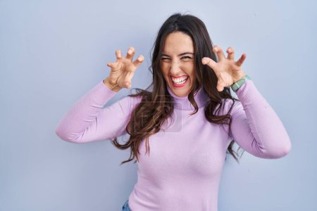 Photo for Young brunette woman standing over blue background smiling funny doing claw gesture as cat, aggressive and sexy expression - Royalty Free Image