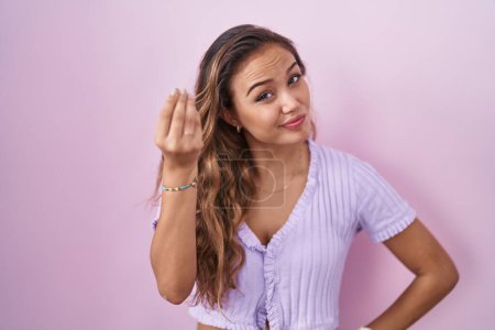 Foto de Mujer hispana joven de pie sobre fondo rosa haciendo gesto italiano con la mano y los dedos expresión confiada - Imagen libre de derechos