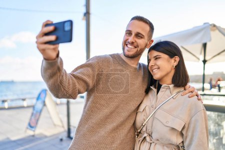 Foto de Hombre y mujer pareja sonriendo confiado haciendo selfie por el teléfono inteligente en la playa - Imagen libre de derechos