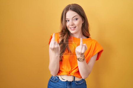 Foto de Caucasian woman standing over yellow background showing middle finger doing fuck you bad expression, provocation and rude attitude. screaming excited - Imagen libre de derechos