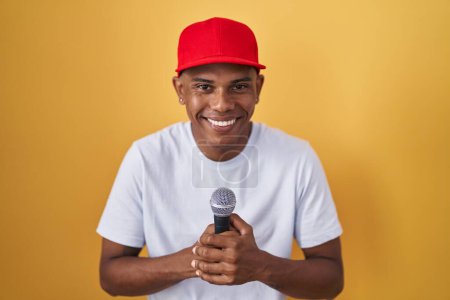 Téléchargez les photos : Jeune homme hispanique chantant chanson en utilisant microphone souriant et riant fort à haute voix parce que drôle blague folle. - en image libre de droit