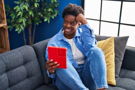 Photo for African american woman using touchpad sitting on sofa at home - Royalty Free Image
