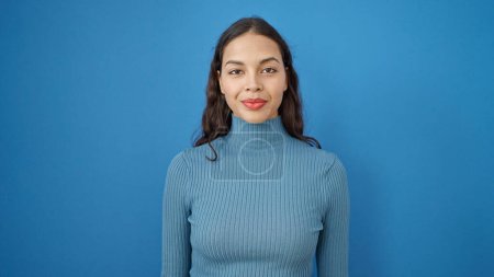 Téléchargez les photos : Jeune belle femme hispanique debout avec une expression sérieuse sur fond bleu isolé - en image libre de droit