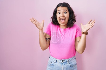 Téléchargez les photos : Jeune femme hispanique debout sur fond rose célébrant fou et étonné pour le succès avec les bras levés et les yeux ouverts hurlant excités. concept gagnant - en image libre de droit
