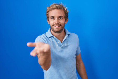 Photo for Caucasian man standing over blue background smiling cheerful offering palm hand giving assistance and acceptance. - Royalty Free Image