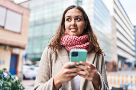 Photo for Young beautiful hispanic woman using smartphone wearing scarf at street - Royalty Free Image