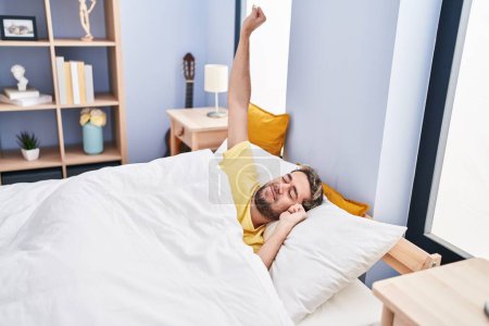 Photo for Young man waking up stretching arms at bedroom - Royalty Free Image