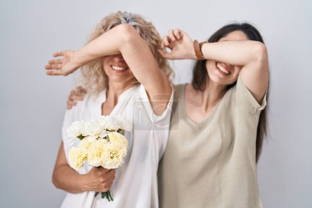 Téléchargez les photos : Mère et fille tenant bouquet de fleurs blanches souriant joyeux jeu jetez un coup d'oeil un boo avec les mains montrant le visage. surpris et sortis - en image libre de droit
