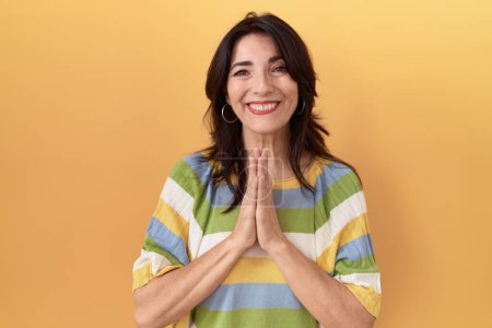 Photo for Middle age hispanic woman standing over yellow background praying with hands together asking for forgiveness smiling confident. - Royalty Free Image
