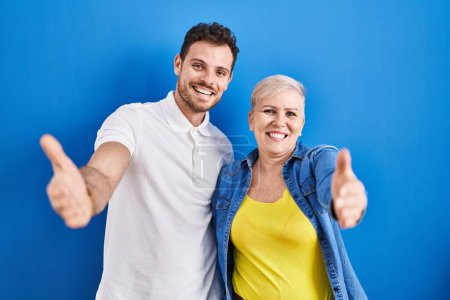 Photo for Young brazilian mother and son standing over blue background looking at the camera smiling with open arms for hug. cheerful expression embracing happiness. - Royalty Free Image