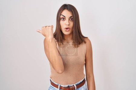 Téléchargez les photos : Jeune femme hispanique debout sur fond blanc surpris pointant du doigt vers le côté, bouche ouverte expression étonnée. - en image libre de droit