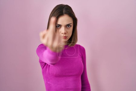 Foto de Hispanic woman standing over pink background showing middle finger, impolite and rude fuck off expression - Imagen libre de derechos