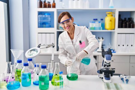 Foto de Middle age woman wearing scientist uniform pouring liquid at laboratory - Imagen libre de derechos