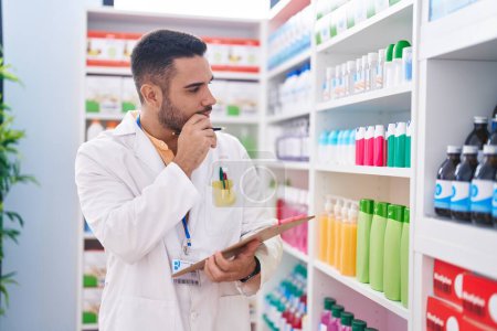 Photo for Young hispanic man pharmacist writing on document with serious expression at pharmacy - Royalty Free Image