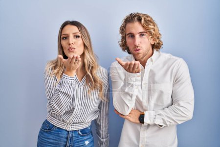 Photo for Young couple standing over blue background looking at the camera blowing a kiss with hand on air being lovely and sexy. love expression. - Royalty Free Image