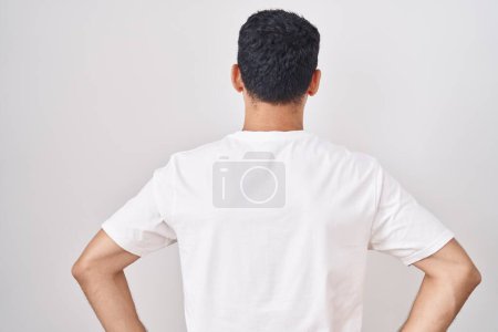 Foto de Hombre hispano guapo de pie sobre fondo blanco de pie hacia atrás mirando hacia otro lado con los brazos en el cuerpo - Imagen libre de derechos