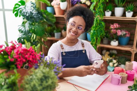 Photo for African american woman florist smiling confident using smartphone at flower shop - Royalty Free Image
