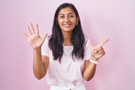 Photo for Young hispanic woman standing over pink background showing and pointing up with fingers number seven while smiling confident and happy. - Royalty Free Image