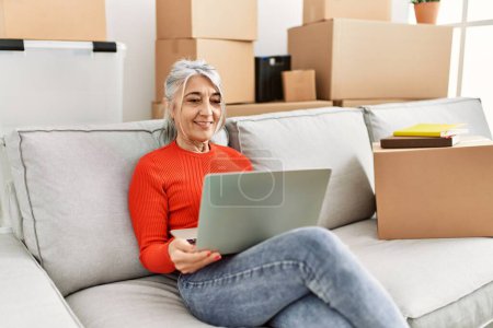 Foto de Mujer de pelo gris de mediana edad sonriendo confiado usando el ordenador portátil en el nuevo hogar - Imagen libre de derechos