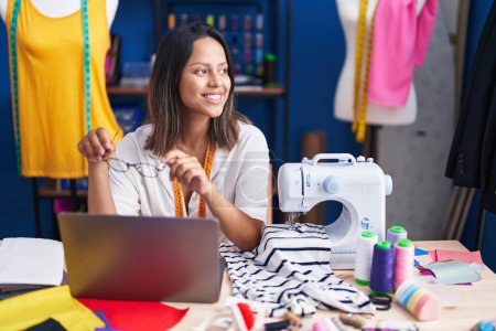 Photo for Young hispanic woman tailor smiling confident using laptop at sewing studio - Royalty Free Image