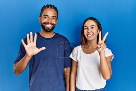 Téléchargez les photos : Jeune couple hispanique debout ensemble montrant et pointant vers le haut avec les doigts numéro sept tout en souriant confiant et heureux. - en image libre de droit