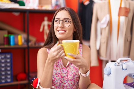 Téléchargez les photos : Jeune belle femme hispanique tailleur souriant confiance boire du café à l'atelier - en image libre de droit